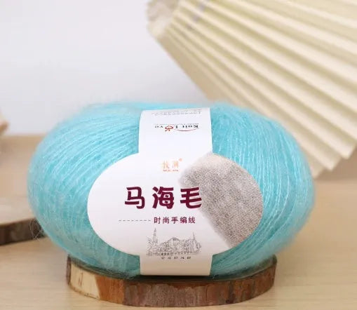 A ball of mohair yarn in a selected colour next to a hand-woven scarf example, showcasing the DIY kit.