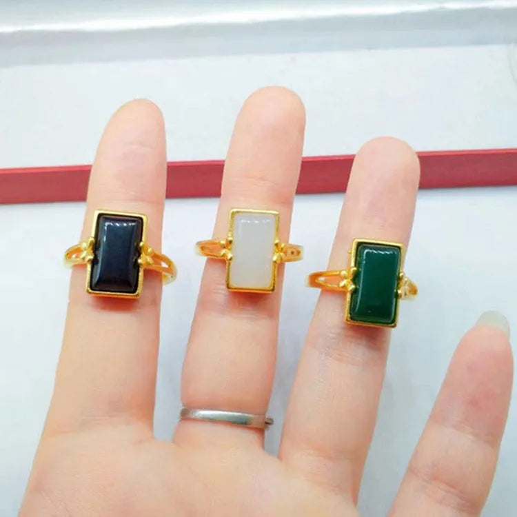 Adjustable brass gold-plated ring with a coloured gemstone inlay on a finger.