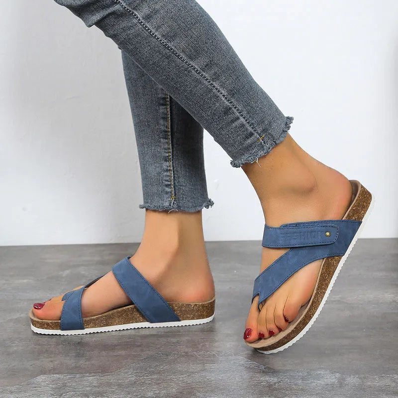 Flat toe ring flip-flops with a thick foam sole in a solid blue colour on a sandy beach.