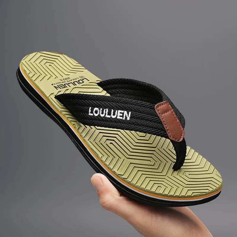 Men's black flip flops with a textured non-slip sole on a sandy beach background.