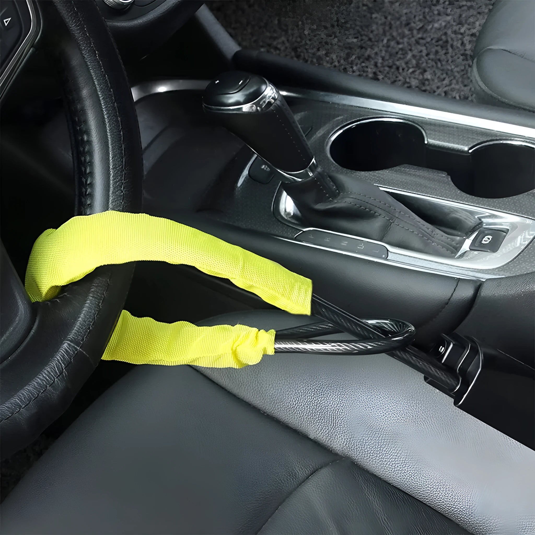 Red car steering wheel lock with iron cable secured around a steering wheel.