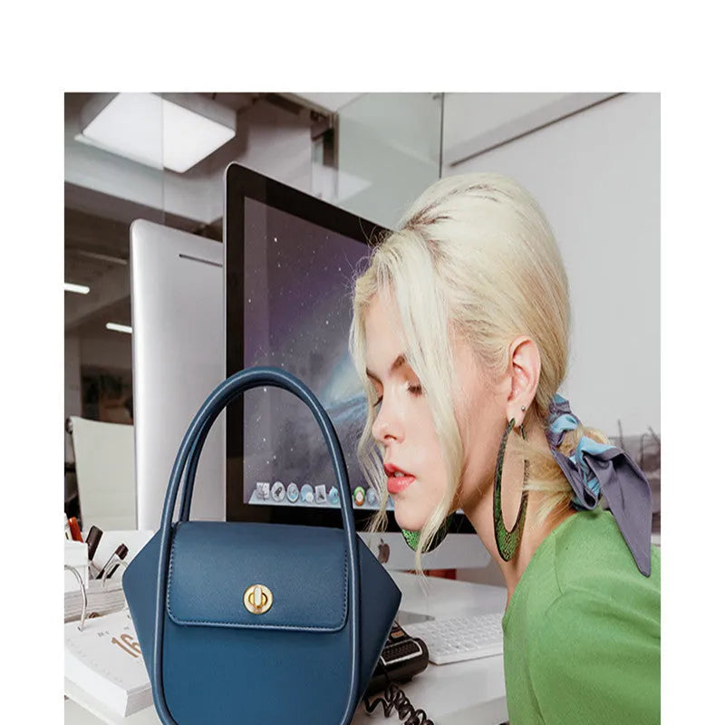 A women's leather wing-shaped tote bag with a metal latch, shown in blue on a cross-body strap.