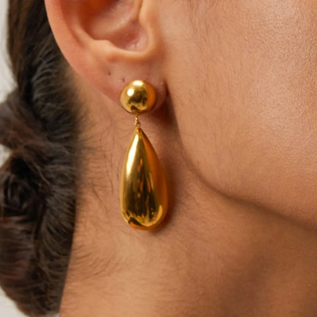A pair of gold-coloured stainless steel pendant earrings with a geometric water drop hemisphere shape.