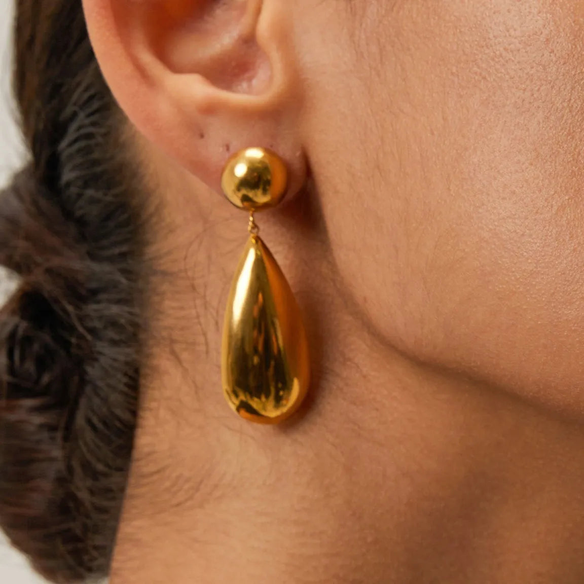 A pair of gold-coloured stainless steel pendant earrings with a geometric water drop hemisphere shape.