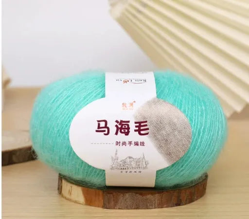 A ball of mohair yarn in a selected colour next to a hand-woven scarf example, showcasing the DIY kit.