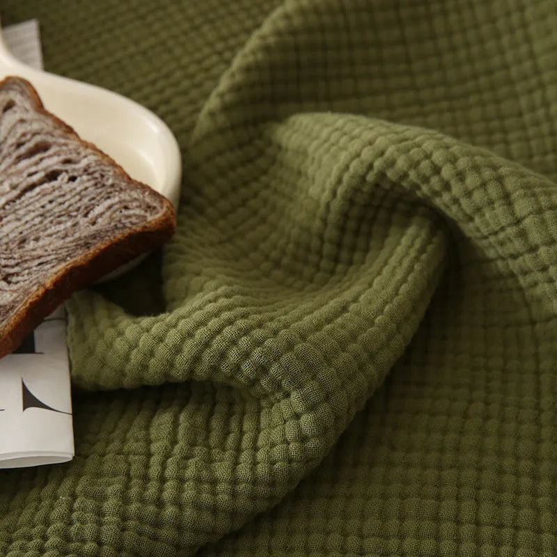 Four-layer gauze cotton blanket with tassel edging in avocado green, laid flat.