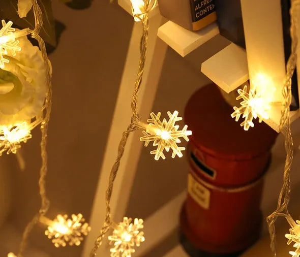 Battery powered LED snowflake string lights in warm white on a garden tree branch for Christmas decoration
