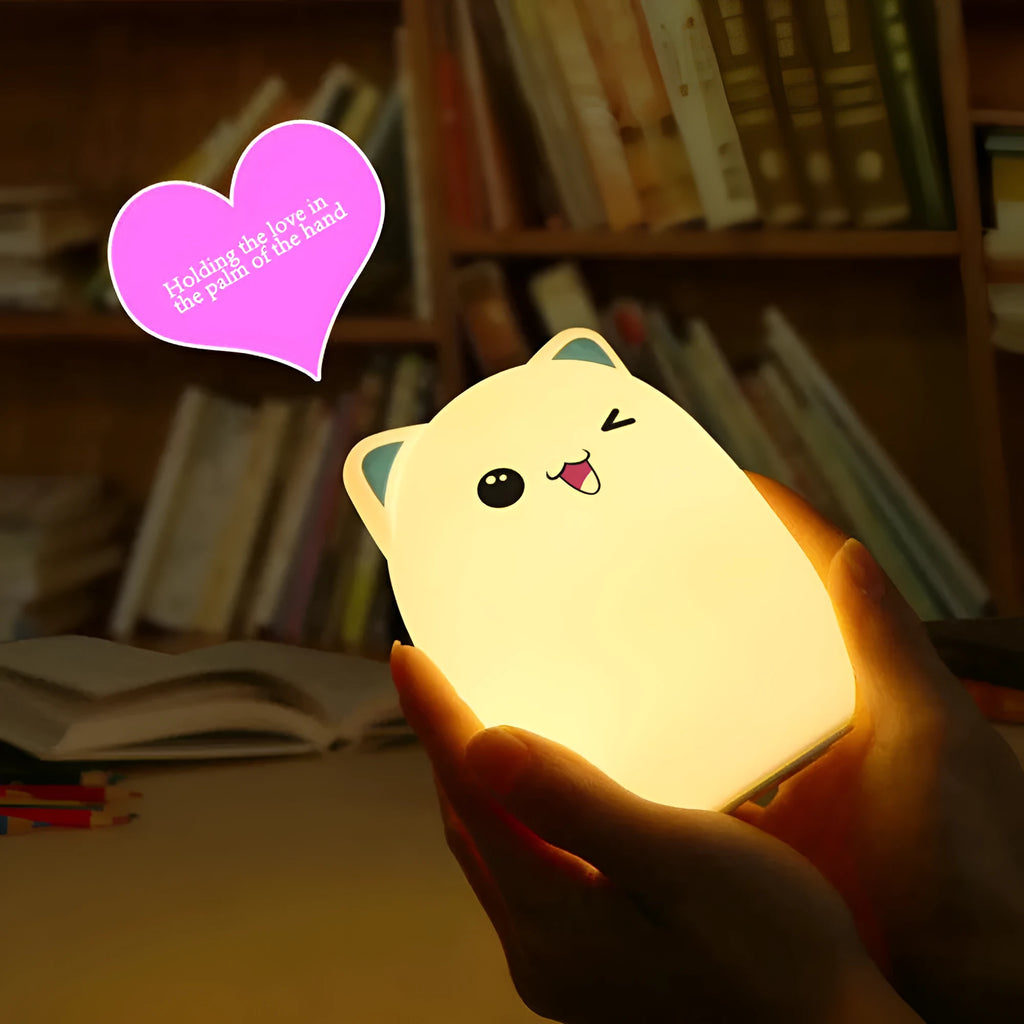 Cartoon silicone clapping night lamp in pink with USB charging cable on a bedside table