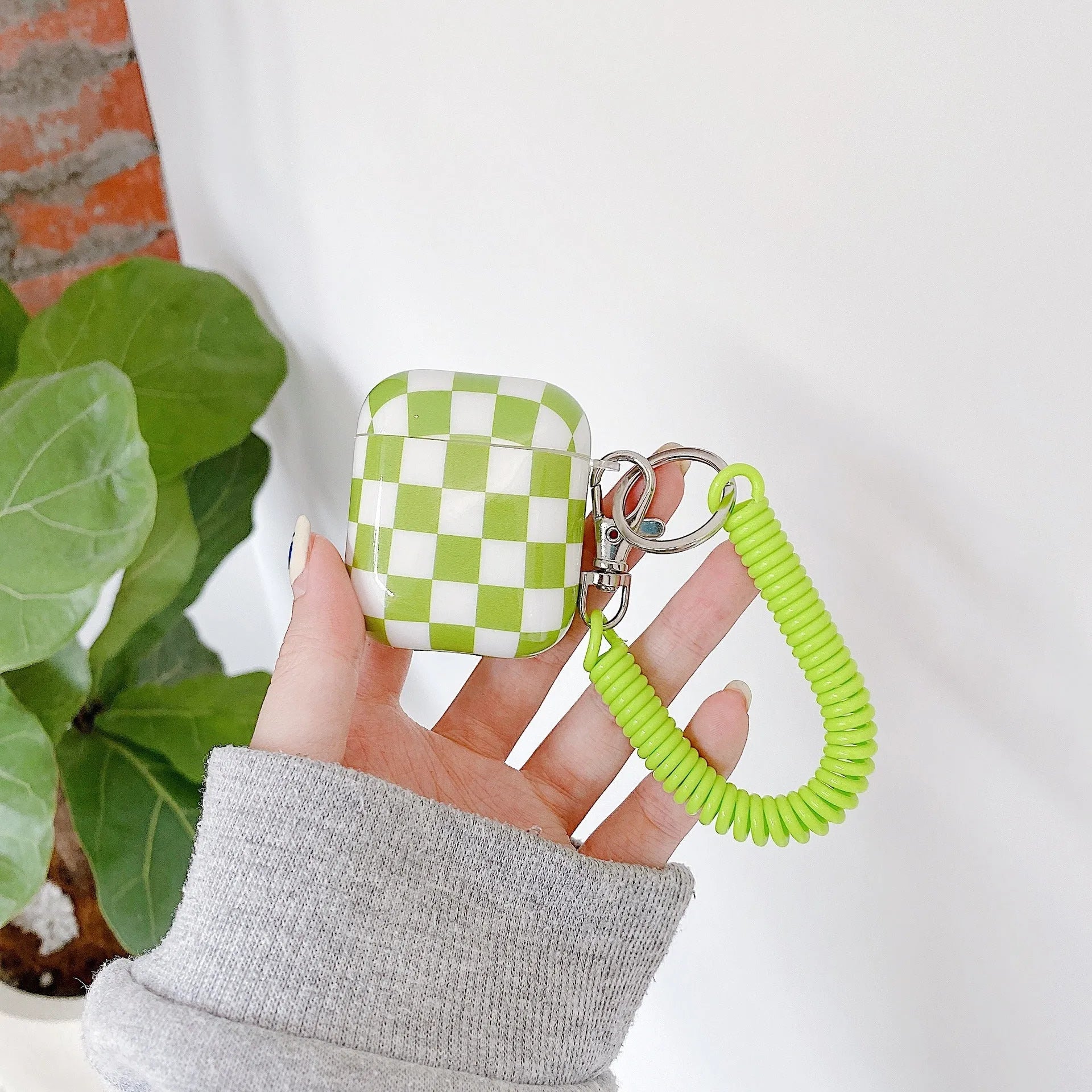 Black and green checkerboard patterned TPU protective case for Apple AirPods with optional lanyard and loop pendant attachments.