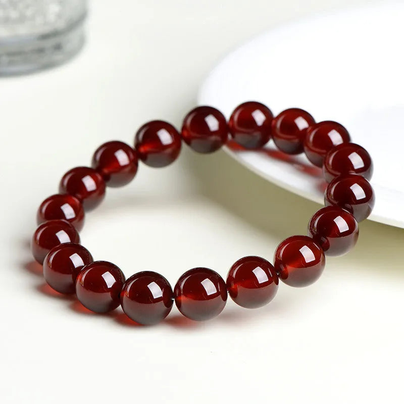 Unisex orange red garnet ball bracelet with crystal beads and a metal Ruyi charm on a wrist.