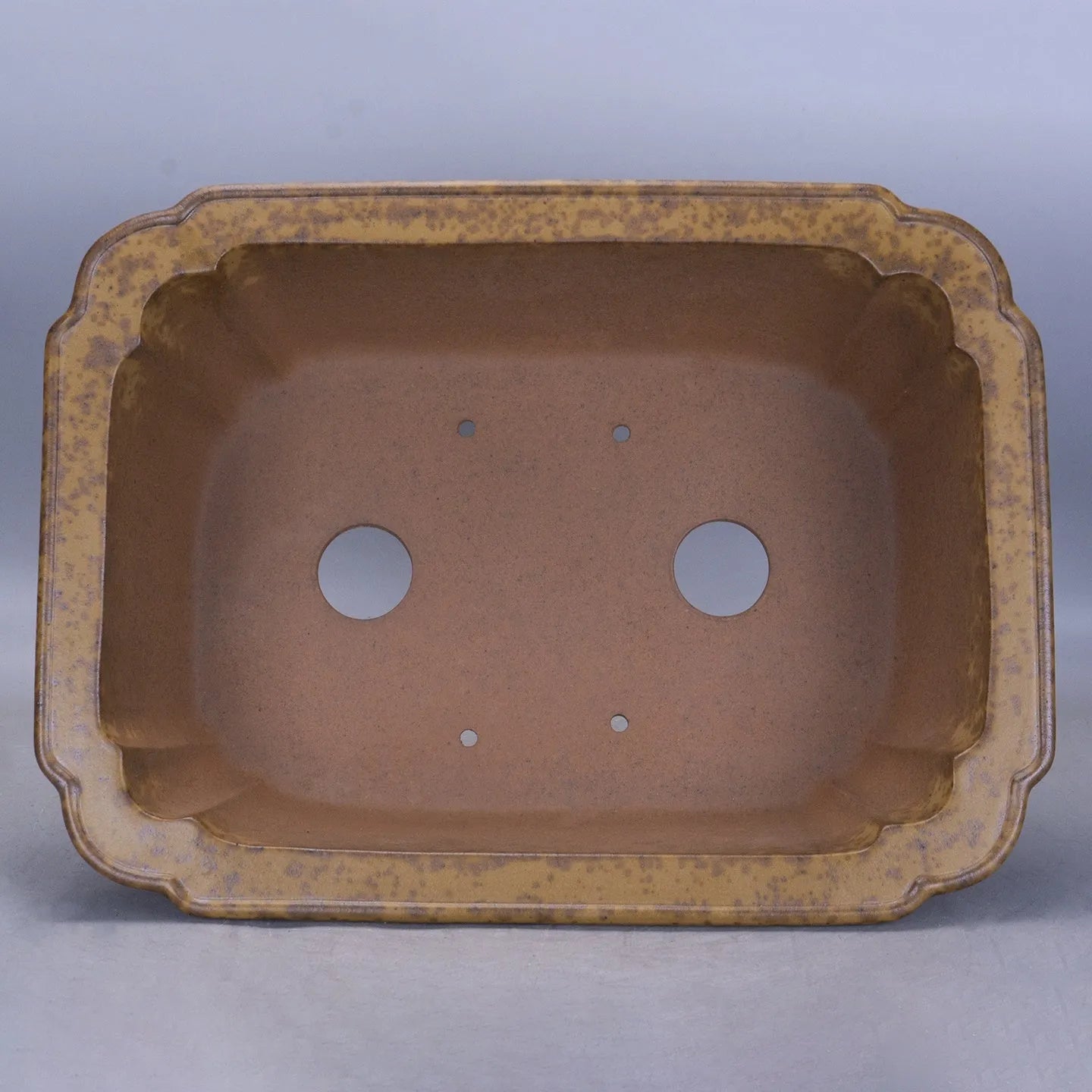 A large, modern rectangular purple sand ceramic flowerpot with sharp angles, shown on a patio.