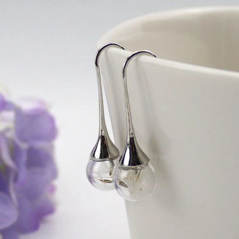 Close-up of a woman's ear wearing 16mm transparent glass ball dandelion seed earrings on a silver French hook.