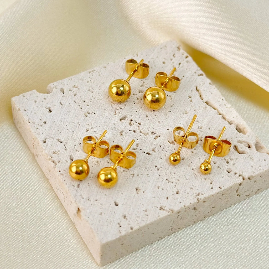 Minimalist round ball stud earrings in gold and silver plating on a white background.