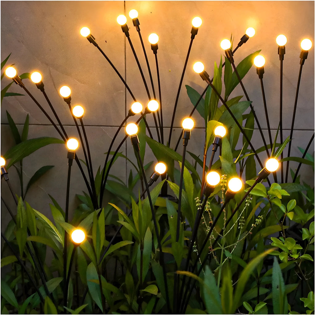 Solar-powered LED garden spike light with multiple glowing heads and a metal ground plug inserted in soil at dusk.