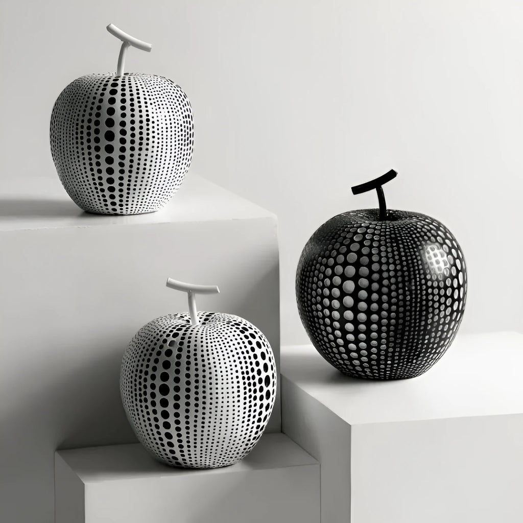 A black resin apple figurine and a white resin pear figurine on a wooden surface.