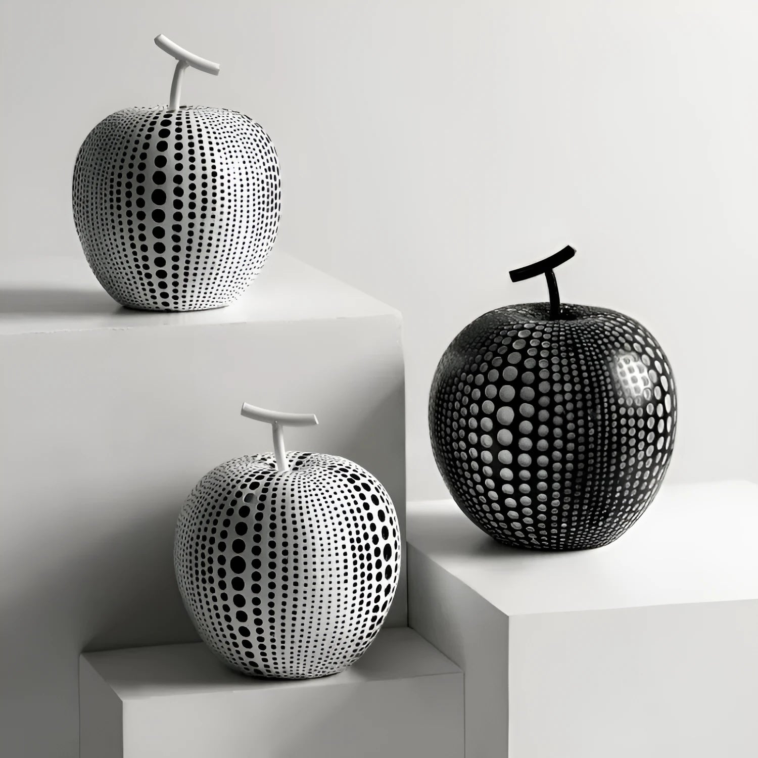 A black resin apple figurine and a white resin pear figurine on a wooden surface.