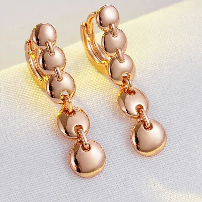 A pair of long, round, woven copper earrings with a gold finish, showing textured detail.