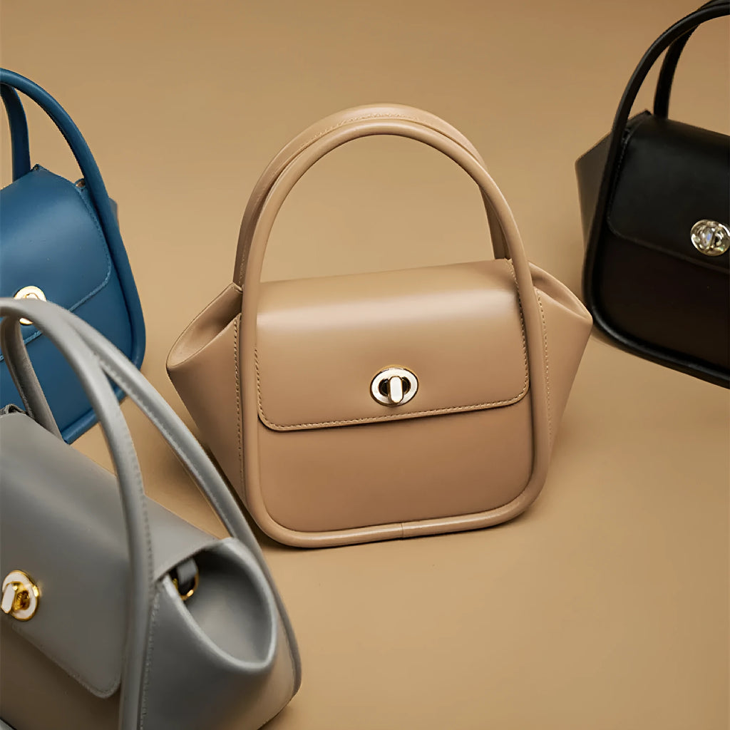 A women's leather wing-shaped tote bag with a metal latch, shown in blue on a cross-body strap.