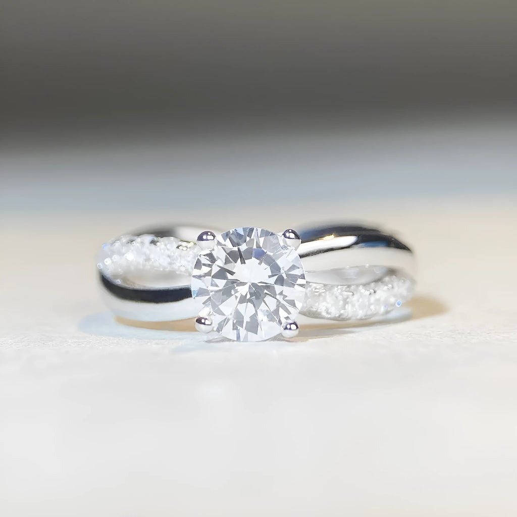 Silver ring with a 1 karat moissanite stone in a twisted four-claw setting, showing geometric lines and a cross design.