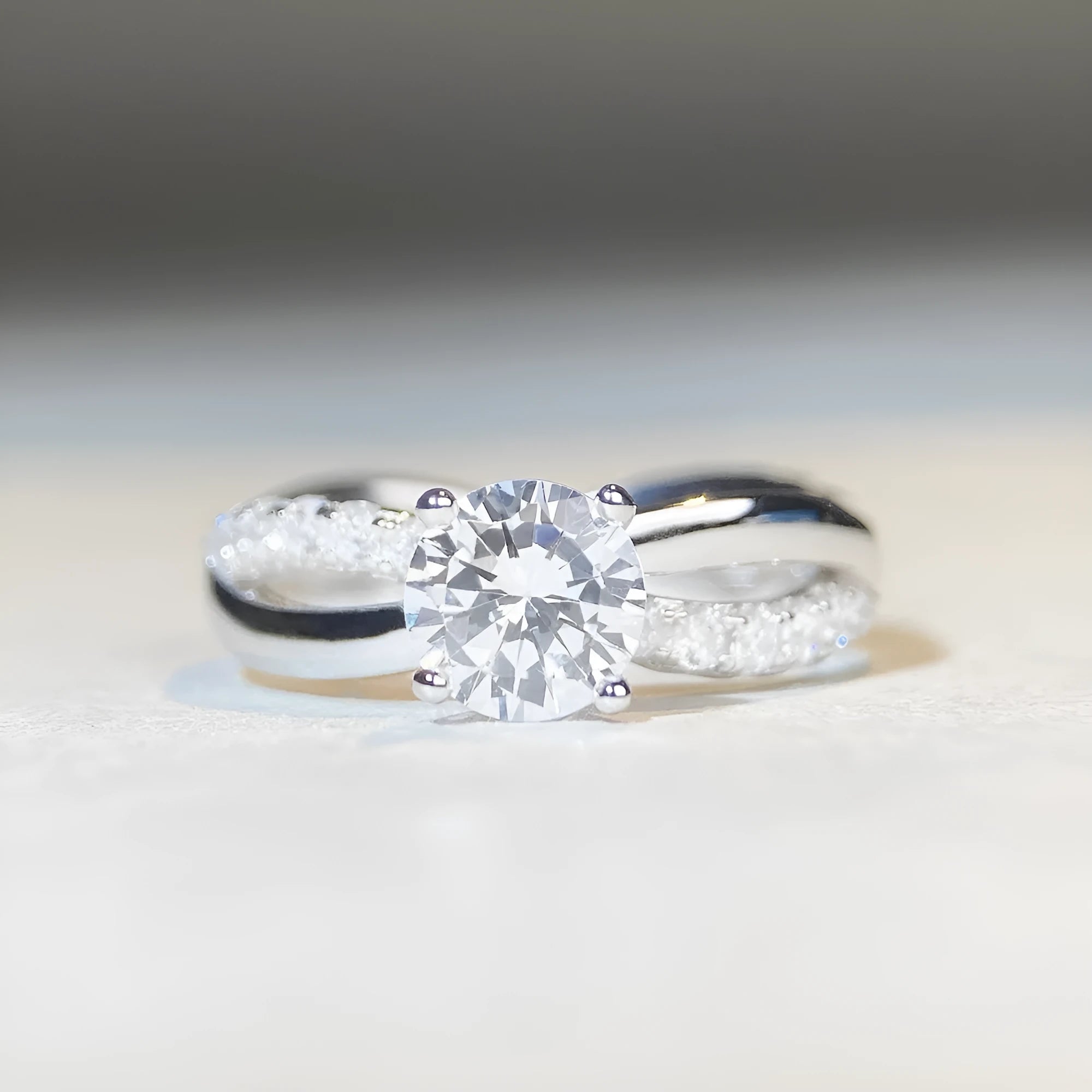 Silver ring with a 1 karat moissanite stone in a twisted four-claw setting, showing geometric lines and a cross design.