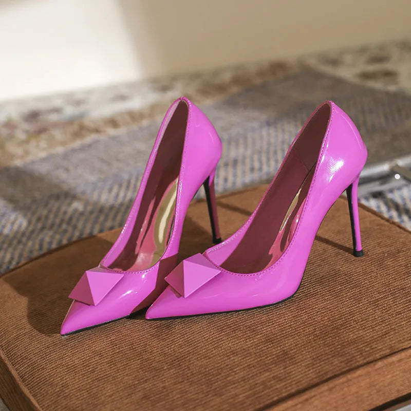 Pink women's pointed toe stiletto high heels with a rivet buckle on a glossy patent leather upper.
