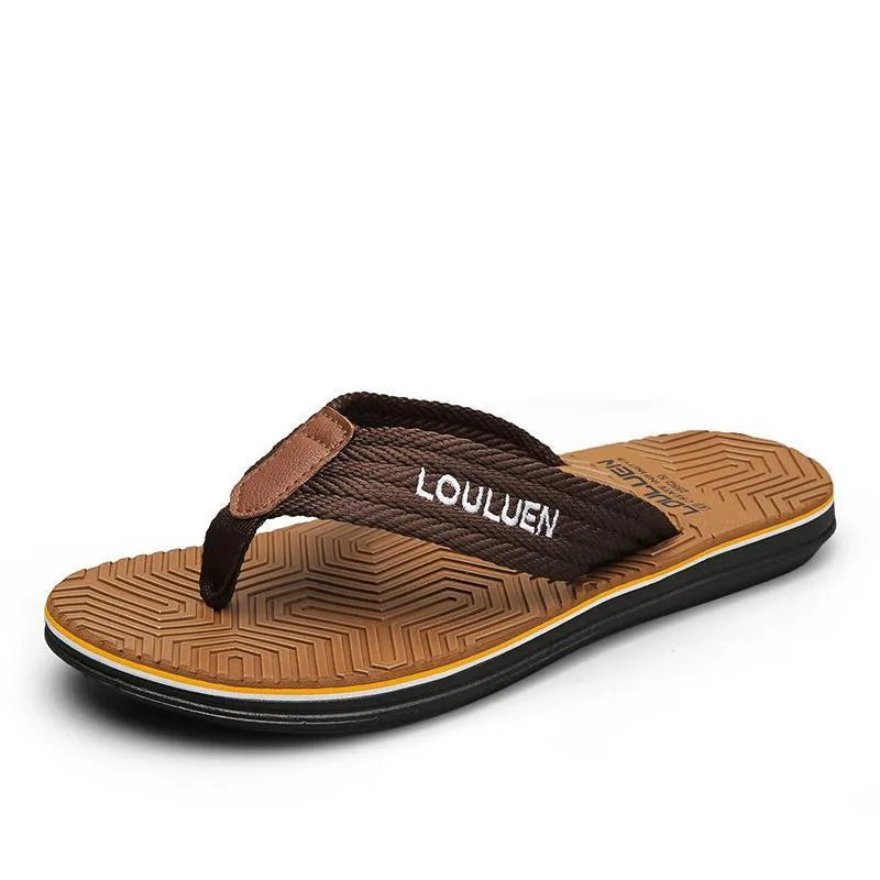 Men's black flip flops with a textured non-slip sole on a sandy beach background.