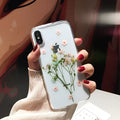 Handmade clear iPhone case with dried pink flowers preserved in epoxy resin visible through TPU back