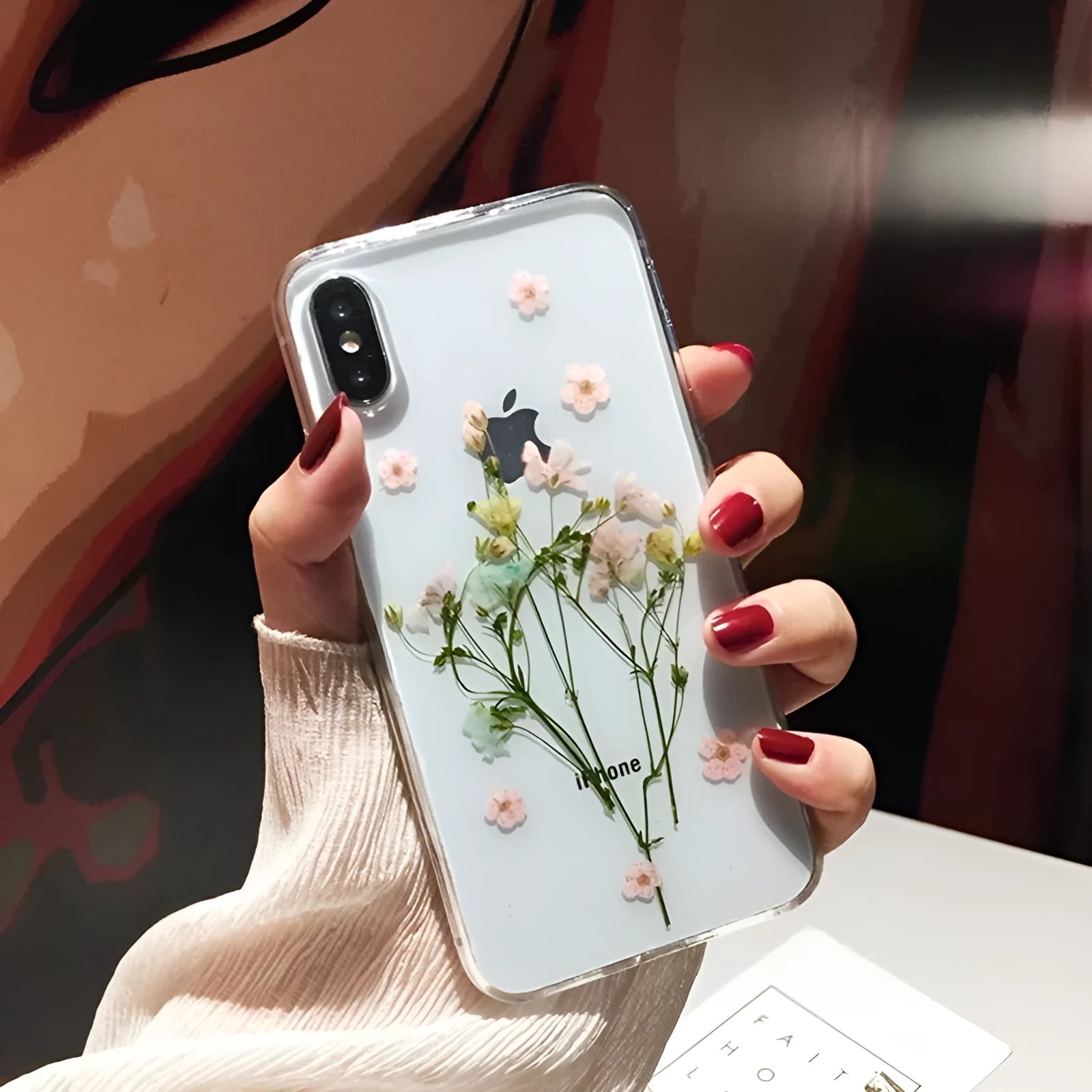 Handmade clear iPhone case with dried pink flowers preserved in epoxy resin visible through TPU back