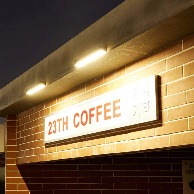 Black solar-powered outdoor wall lamp with integrated solar panel, mounted on a garden wall.