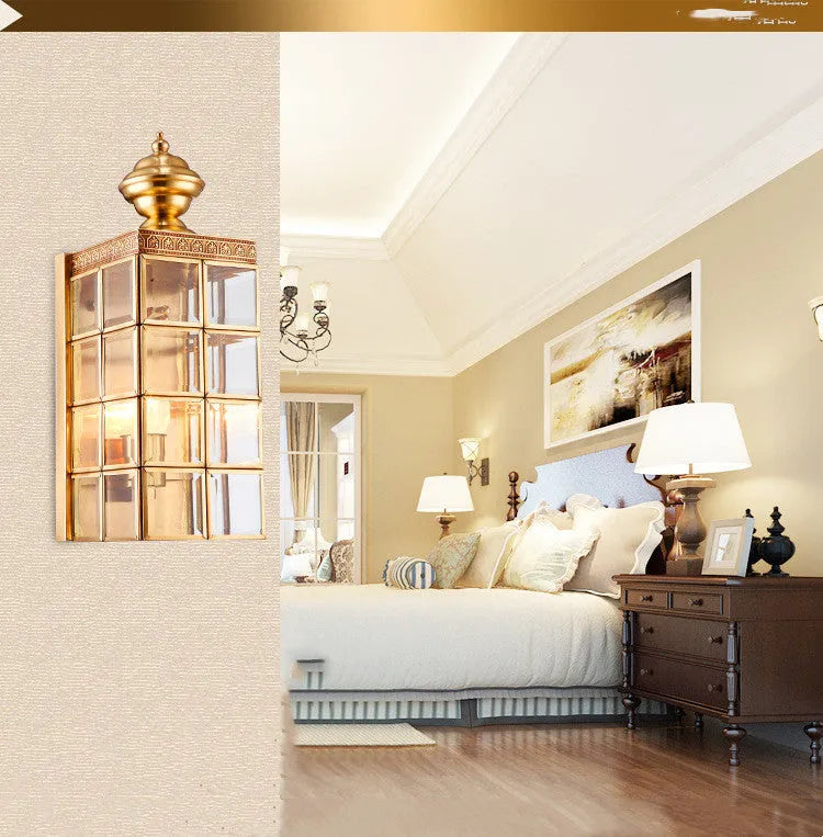 Full copper wall lamp with glass shade and gold finish on a brick balcony wall