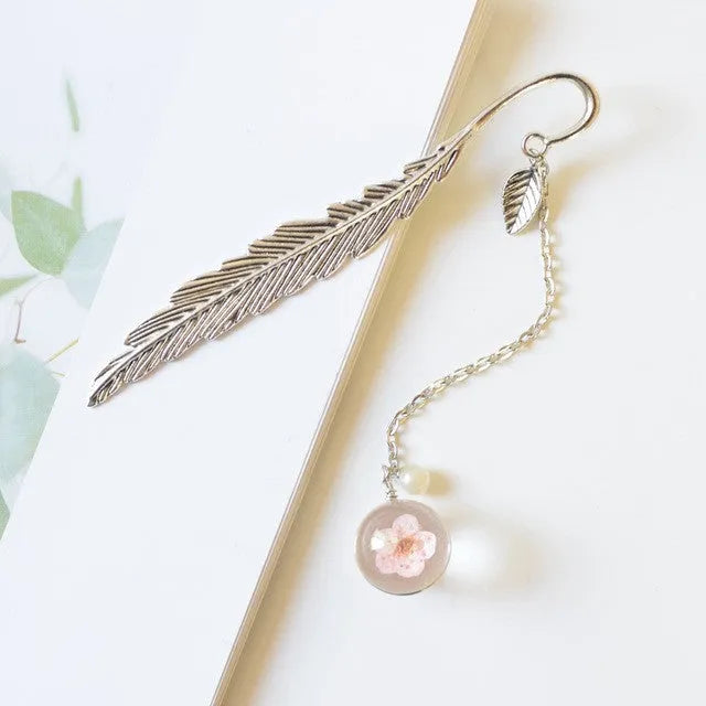 Flat metal bookmark with a dried flower inside, showing colour options like blue starry sky and dandelion.