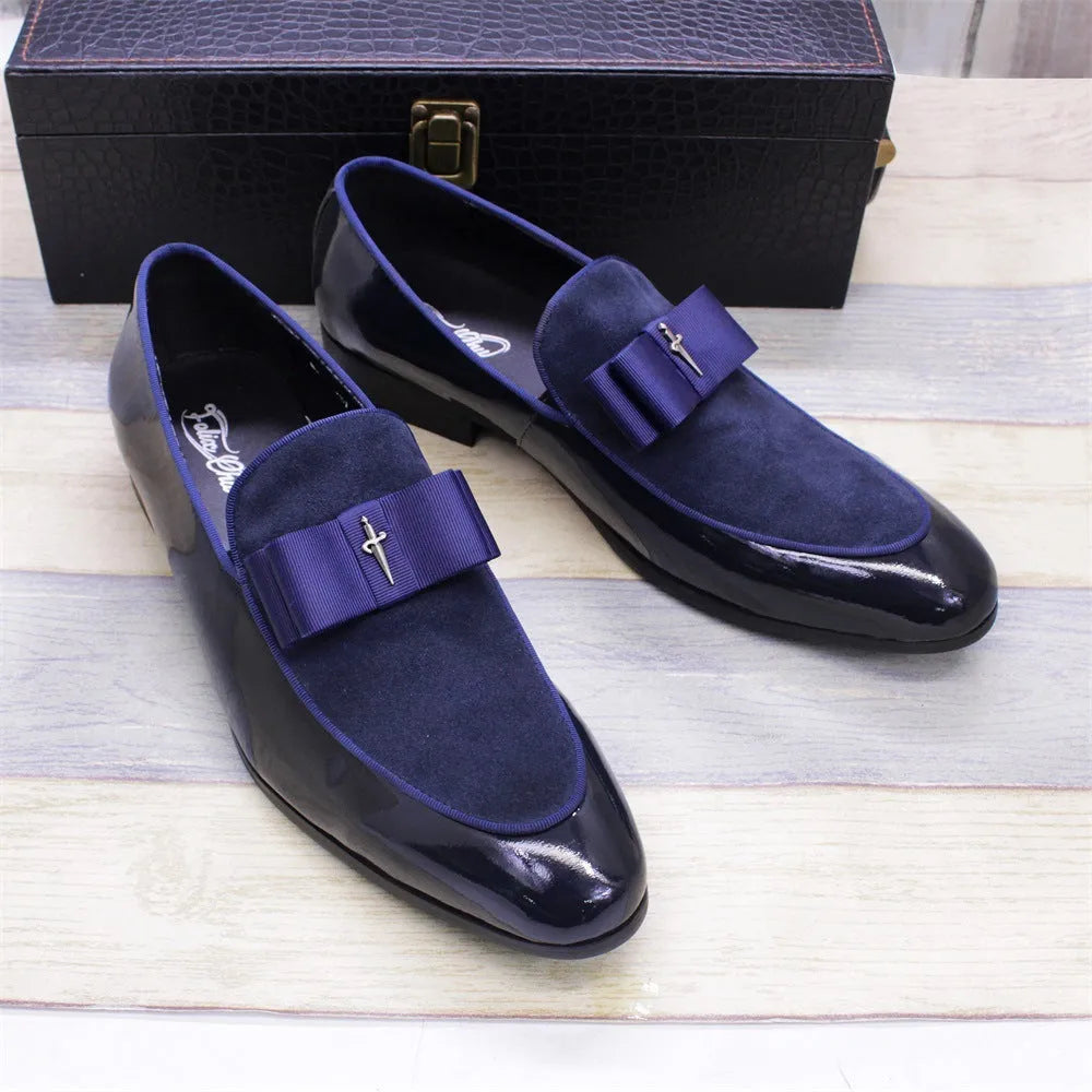 Men's black tassel loafers with glossy patent leather upper and matte leather toe holder on a wooden floor.