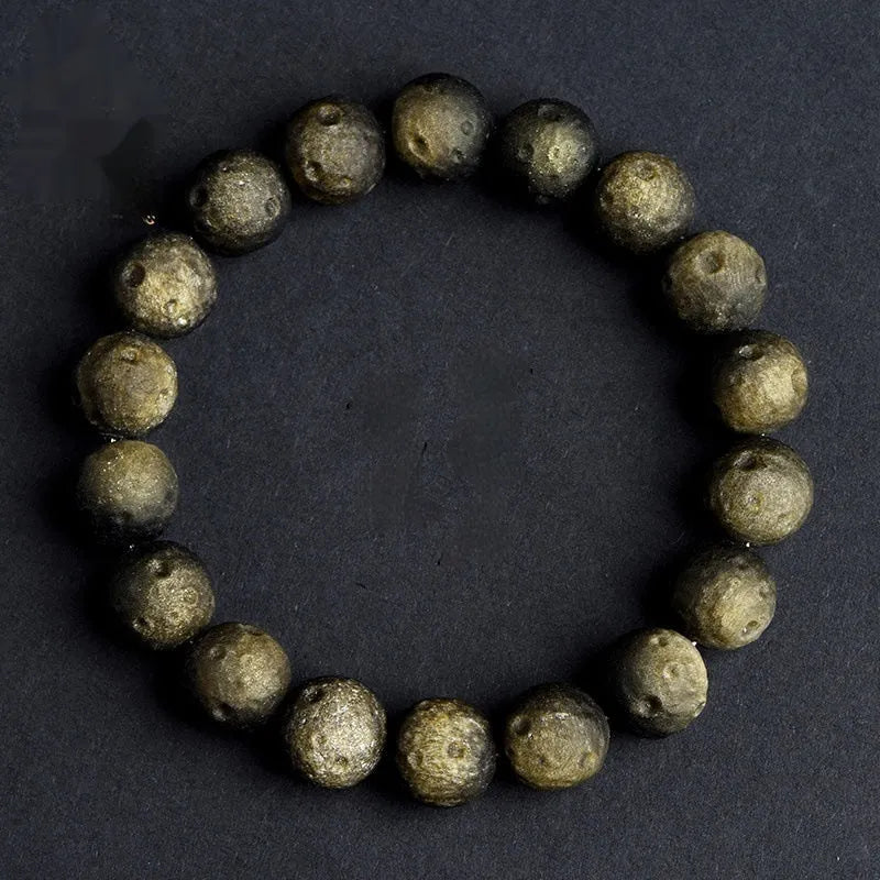 A natural obsidian crater ball bracelet in gold or silver meteorite colour on a wrist, showing textured bead detail.