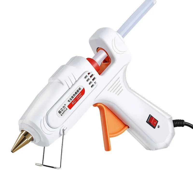 White electric hot glue gun with a metal stand and anti-heat blanket on a table.