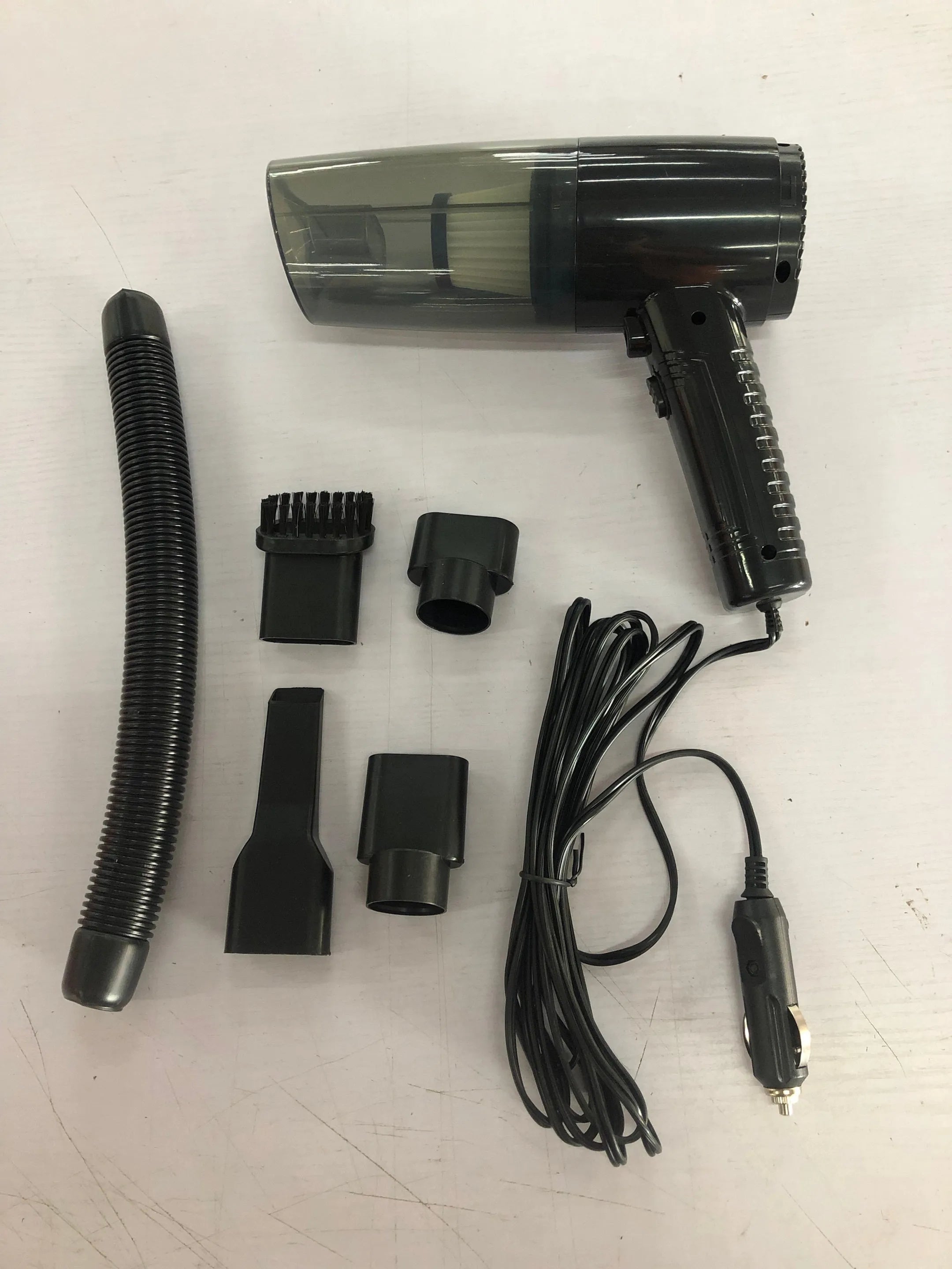 Black and white mini car vacuum cleaner with long cable and suction head accessories on a table.