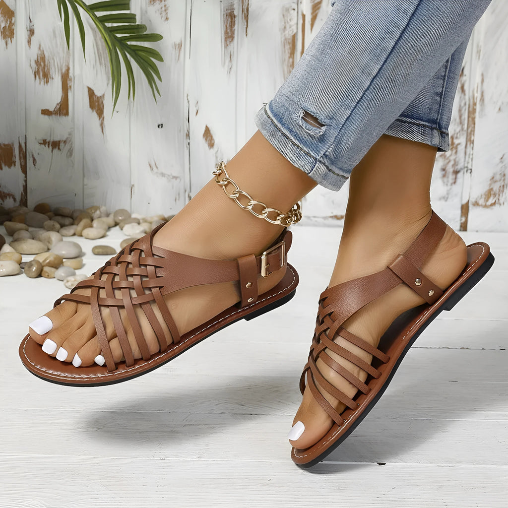 Black Roman style beach slippers with a cross strap and flat buckle closure on a lightweight PU leather upper.