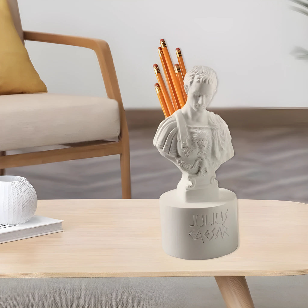 White resin sculpted character pen holder on a desk, holding pens and pencils.