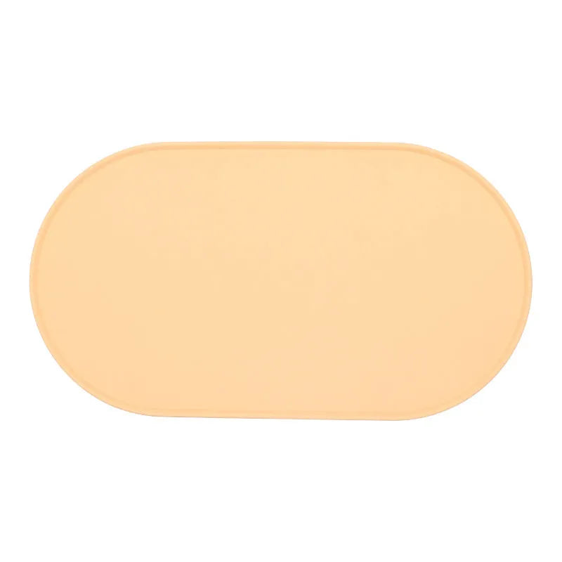 Green silicone cat feeding mat with raised edge under a ceramic food and water bowl on a wooden floor.