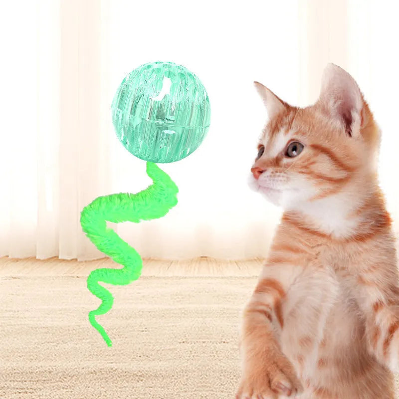 Green bouncy worm-shaped cat toy with a long plush tail on a wooden floor.