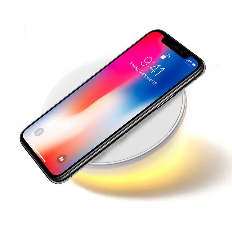 White wireless charging pad with digital clock display and night light, shown on a wooden surface.