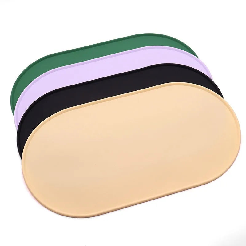 Green silicone cat feeding mat with raised edge under a ceramic food and water bowl on a wooden floor.