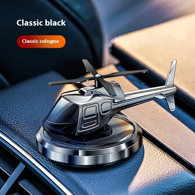 Silver metal solar helicopter car perfume ornament with rotating blades on a dashboard.