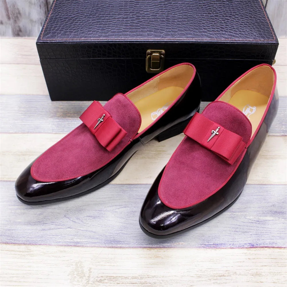 Men's black tassel loafers with glossy patent leather upper and matte leather toe holder on a wooden floor.