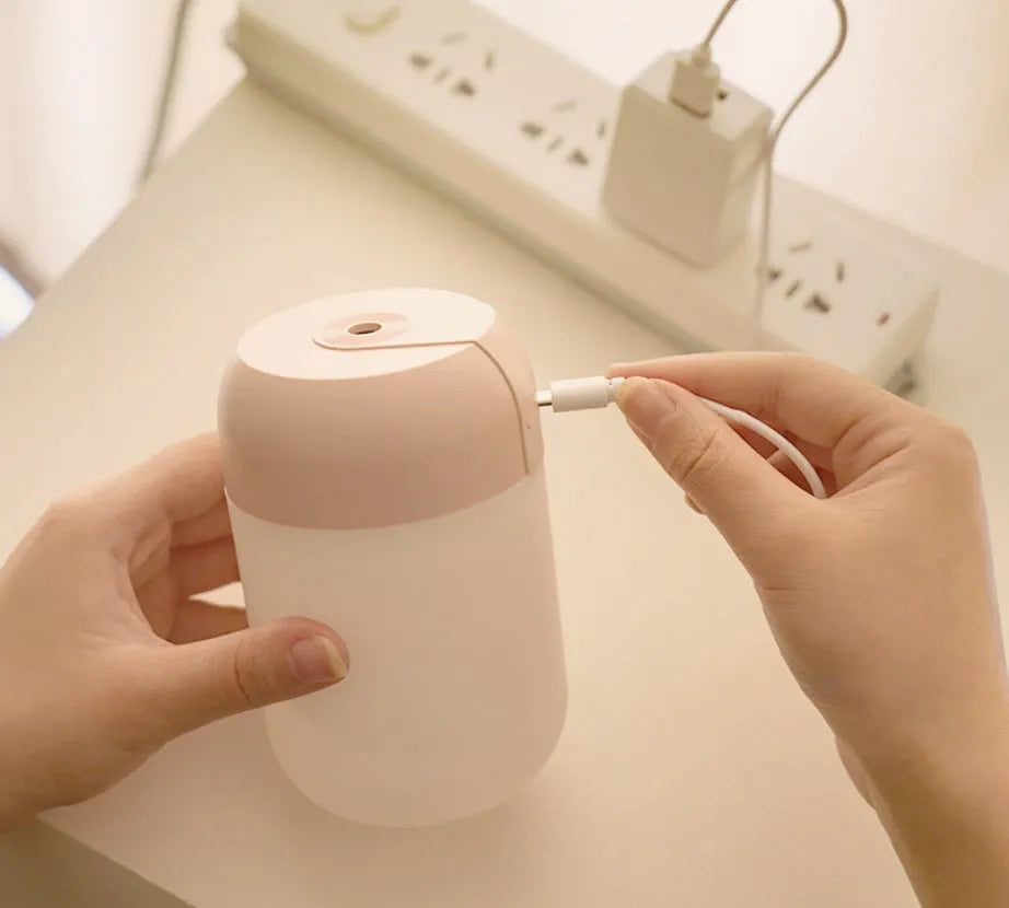 White cylindrical mini USB humidifier on a wooden desk next to a laptop.