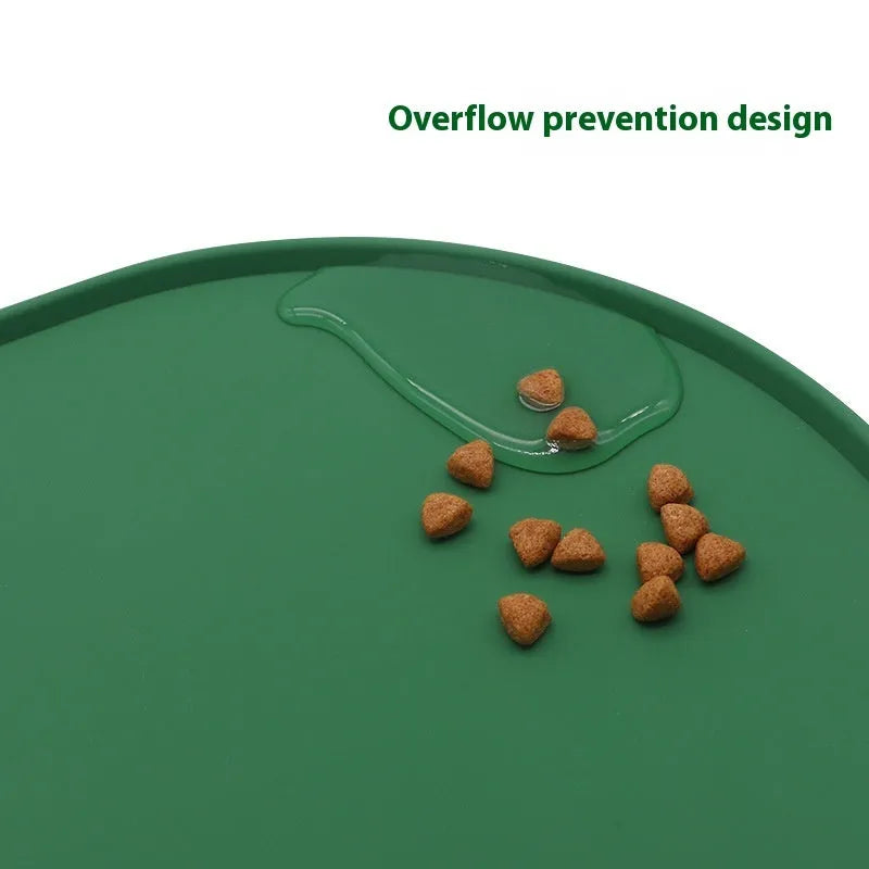 Green silicone cat feeding mat with raised edge under a ceramic food and water bowl on a wooden floor.