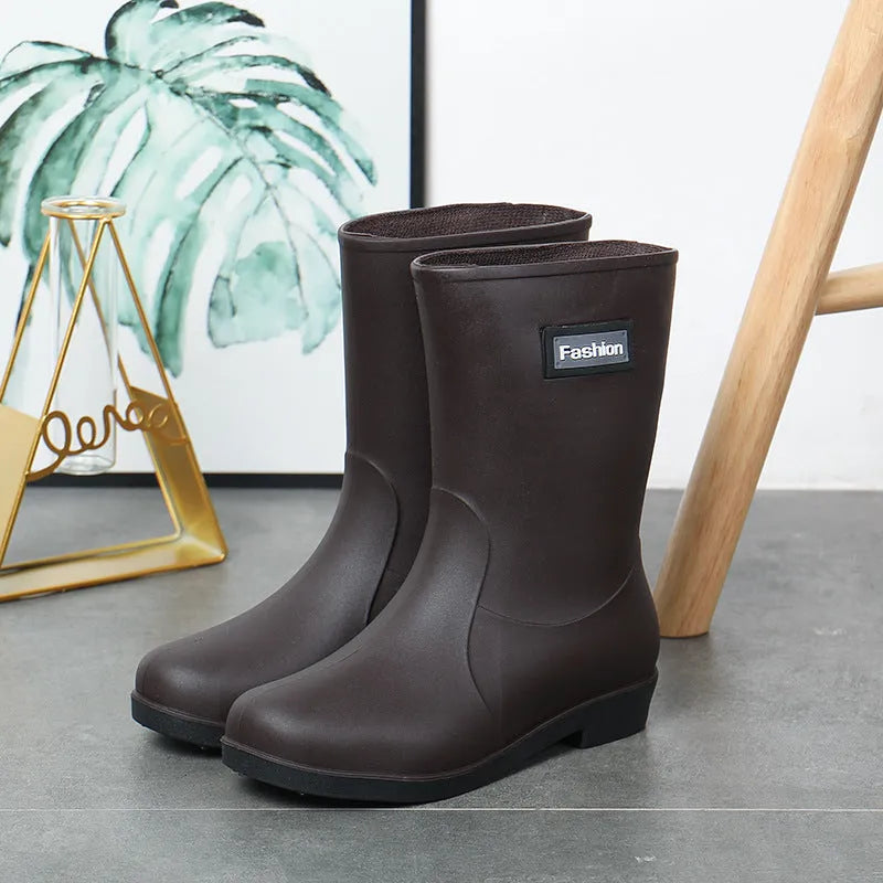 Women's black PVC mid-calf rain boot with a low heel on a wet surface.