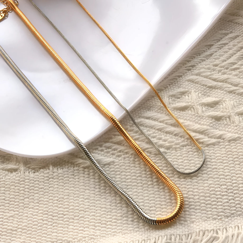 Gold-coloured snake bone chain necklace with geometric links on a white background.