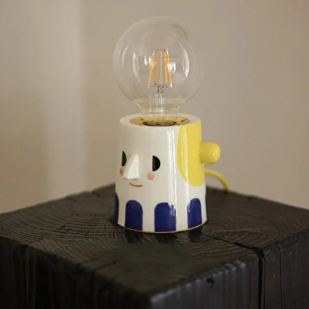 Handmade ceramic bedside lamp with a white ball headlight on a wooden table.