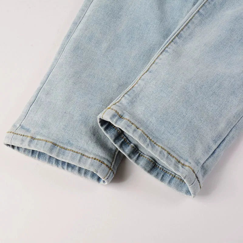 Light blue slim fit men's jeans with patch details, holes, and enzyme-washed finish