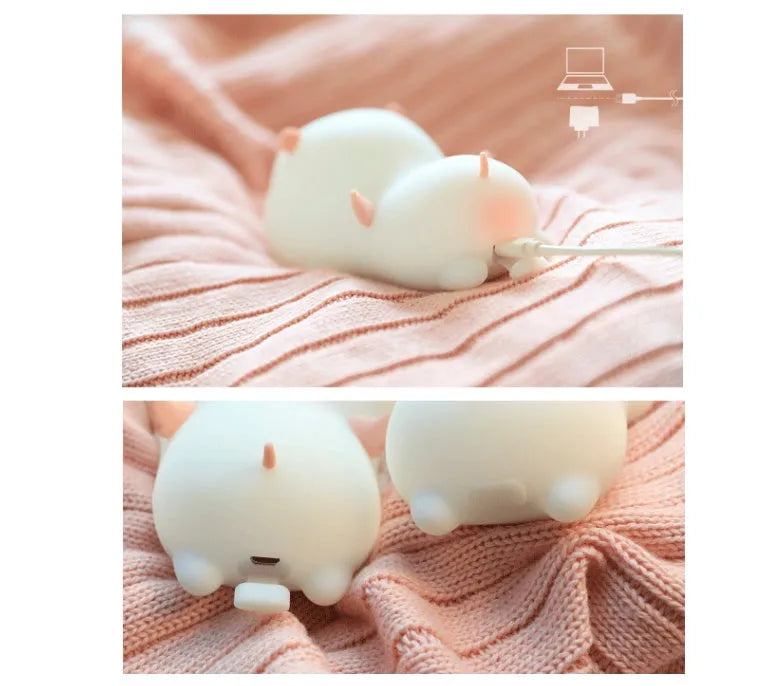 Blue rechargeable pig-shaped silicone night light with soft glow on a bedside table.